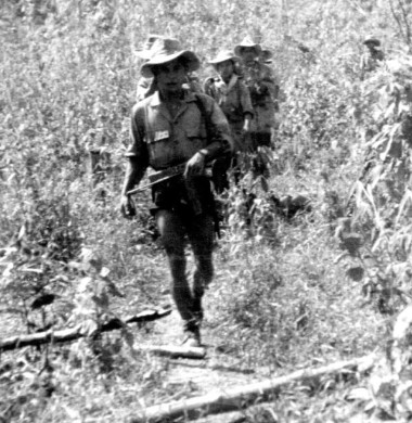 Parachutistes LAO en colonne dans une bambouseraie .Vu de face le premier homme armé d'un P.M. Mat 49 porte une chemise qui fait penser à la tenue de jungle anglaise (1944 ) mais pourrait tout aussi bien avoir été confectionnée localement .